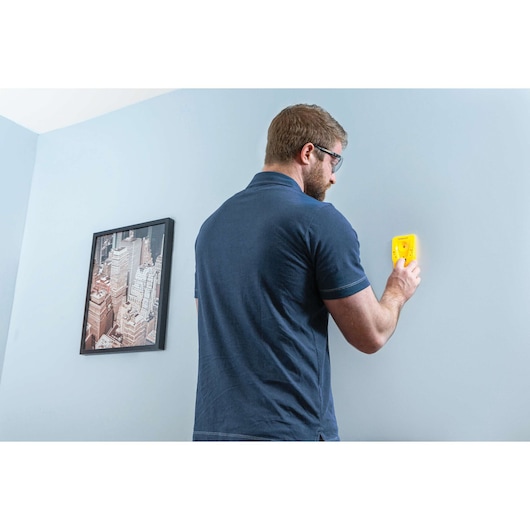 STANLEY STHT77587 stud finder held against blue wall in home setting, man using device.