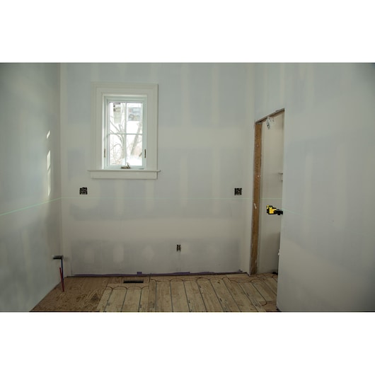 STANLEY STHT77594-1 laser level projecting a green line across an unfinished room, mounted on the right wall.