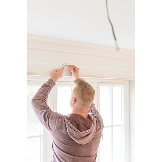 STANLEY STHT77594-1 laser level marking a straight line on a wall in a bright indoor setting.