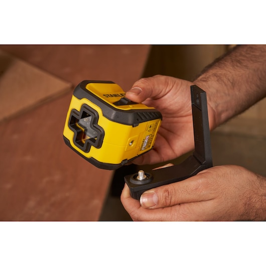 STANLEY STHT77611-0 yellow laser level held in hands with mounting bracket, photography close-up.
