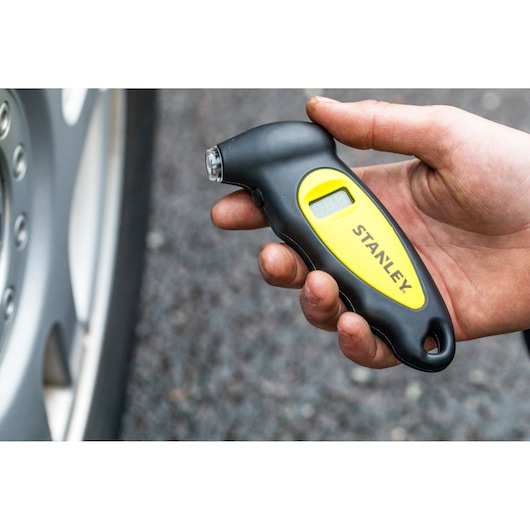 Stanley STHT80874-0 digital tire pressure gauge handheld near car wheel, black and yellow design.