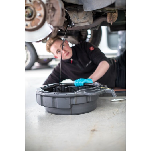 Photo of STANLEY STHT80878-1 oil drain pan under car collecting oil, mechanic wearing blue glove visible.