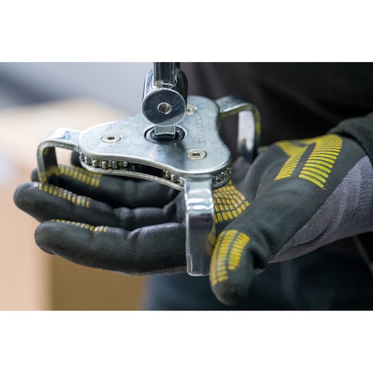 Photo of STANLEY STHT80880-0 adjustable oil filter wrench held in gloved hands, close-up view.