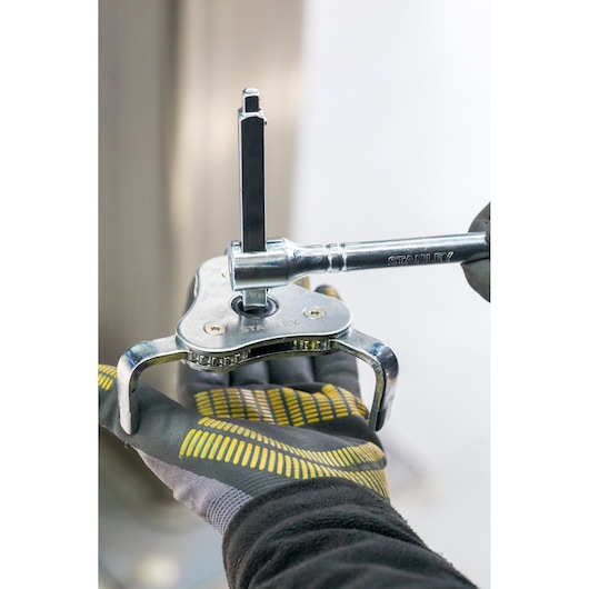 STANLEY STHT80880-0 adjustable three-jaw puller tool in use, close-up showing gloved hand.
