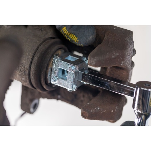STANLEY STHT80883-0 brake caliper tool in use on rusty car brake assembly, close-up view.