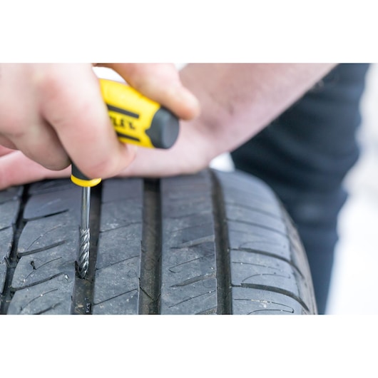 STANLEY STHT80891-0 tire repair tool in use on a car tire tread, close-up photography.
