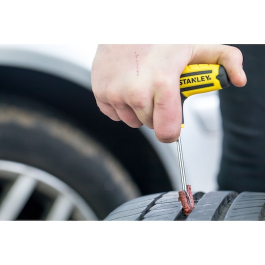 STANLEY STHT80891-0 tire repair tool in use on a car tire, close-up photography.