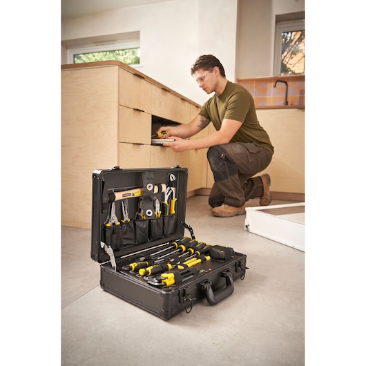 STANLEY STMT72986-1 tool case with assorted hand tools on floor in modern kitchen, person working on cabinet.