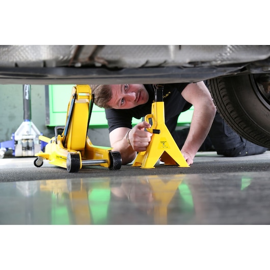 Photo of STANLEY STMT81255-1 yellow car jack and stand under vehicle, automotive tool usage scene.