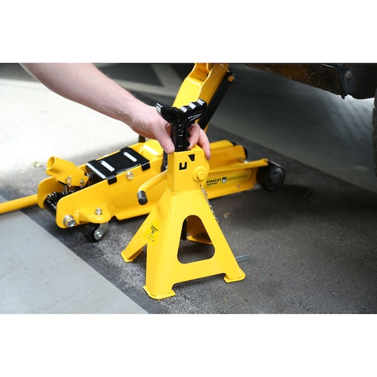 Photo of STANLEY STMT81255-1 yellow jack stand being set under a vehicle, with a floor jack in the background.
