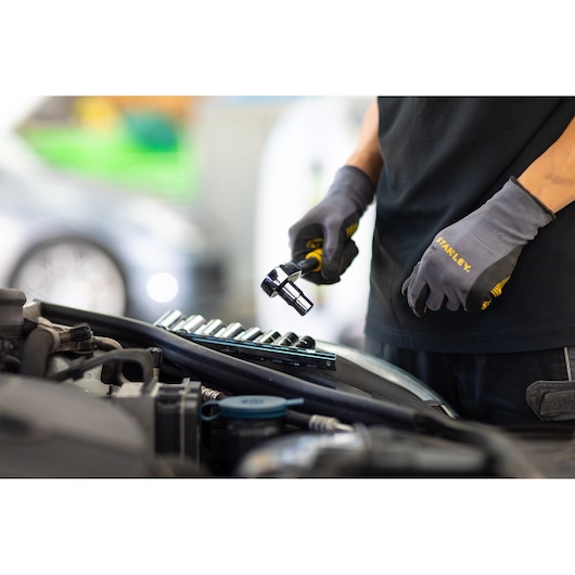 Stanley STMT82666-0 mechanic using ratchet and socket set next to car engine, close-up view.