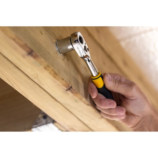 STANLEY STMT82666-0 ratchet wrench used on a wood beam, close-up with yellow and black handle.