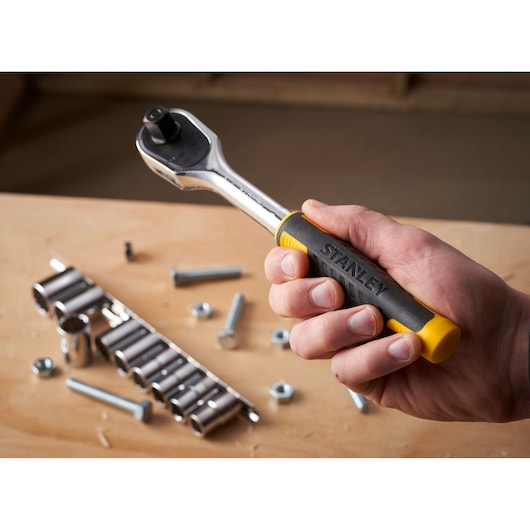 STANLEY STMT82671-0 ratchet wrench with black and yellow handle, held in hand, socket set in background.
