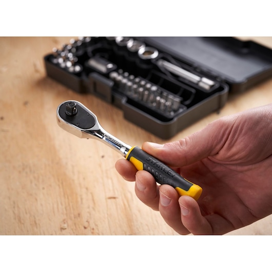 STANLEY STMT82672-0 ratchet wrench with black and yellow grip held in hand, tool kit in background.