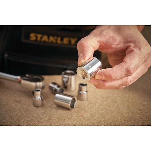 STANLEY STMT86313-0 socket set photography, hand holding chrome socket, tools on workbench.