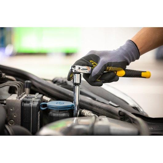 STANLEY STMT86407-0 ratchet wrench in use by gloved hand tightening bolt on car engine, side angle.