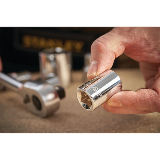 STANLEY STMT86512-0 chrome socket being held by hand, ratchet wrench and other sockets in background, close-up.