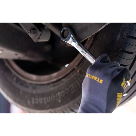 Stanley STMT89911-0 ratcheting wrench in gloved hand tightening bolt on car wheel, close-up photo.