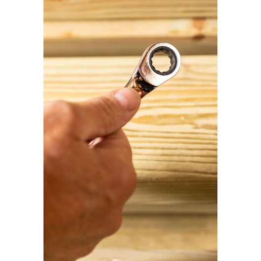 STANLEY STMT89915-0 ratcheting wrench held in hand, close-up against wooden background, photography.