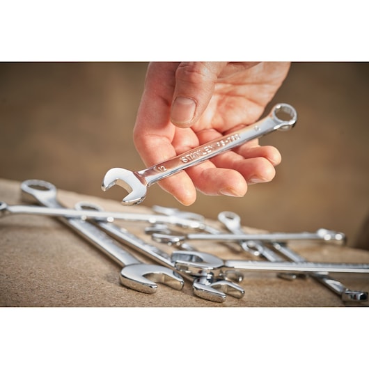 Photo of a hand holding a STANLEY STMT95792-0 combination wrench with other wrenches on a work surface.