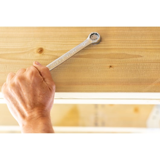 Stanley STMT95911-0 wrench held by hand tightening bolt on wooden surface, close-up photography.