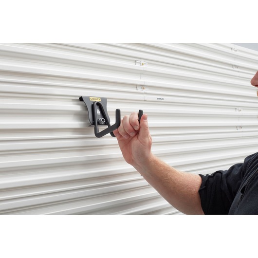 Photo of STANLEY STST82607-1 wall hook being mounted on white grooved panel, close-up view.