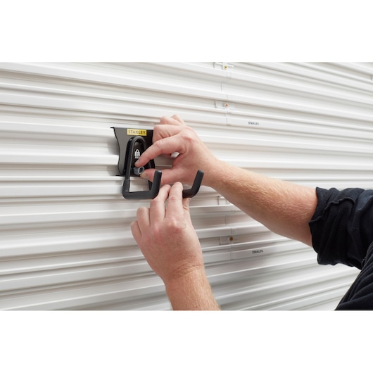 Photo of STANLEY STST82607-1 double hook being mounted on white slatwall, hands adjusting the black hook.