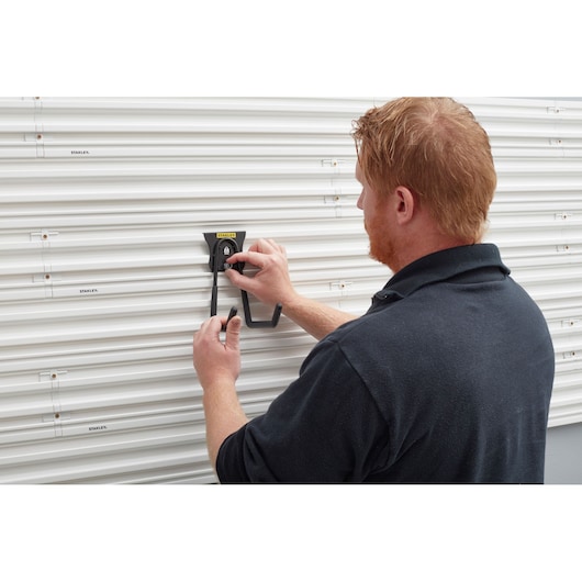Photo of STANLEY STST82608-1 wall hook being installed on white slat wall panel, storage accessory in use.