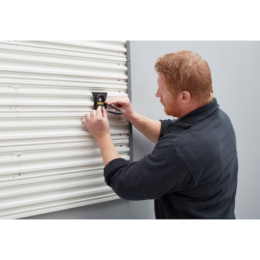 Stanley STST82616-1 wall hook being installed on a white corrugated wall by a person.