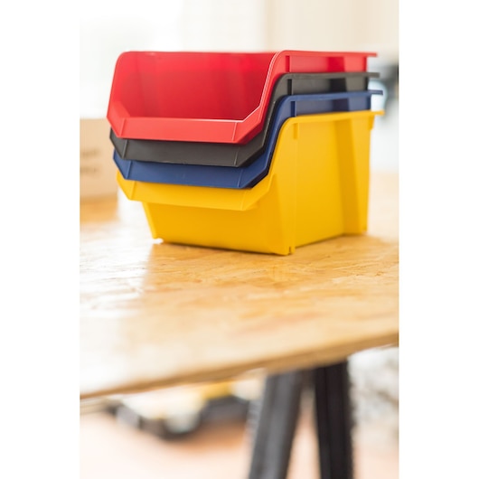 STANLEY STST82739-1 stackable plastic storage bins in red, black, blue, and yellow on a wooden table, side angle.