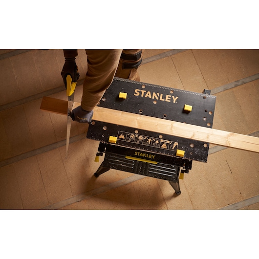 STANLEY STST83800-1 workbench in use, holding wood for sawing, photographed from above on workshop floor.