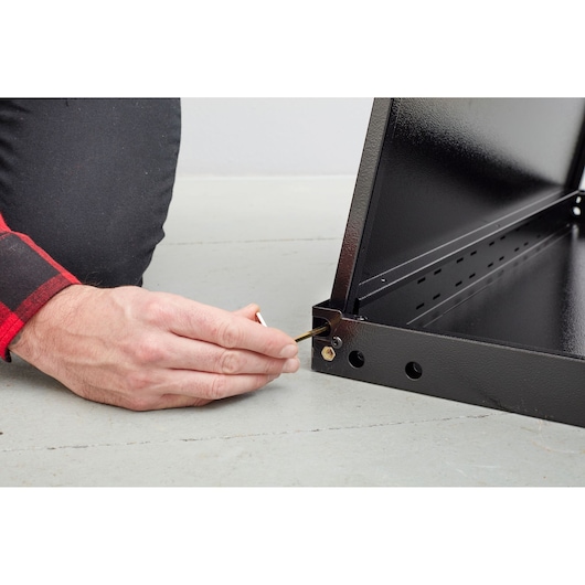 STANLEY STST97595-1 person assembling black metal frame with hex key, close-up on hand and corner joint.