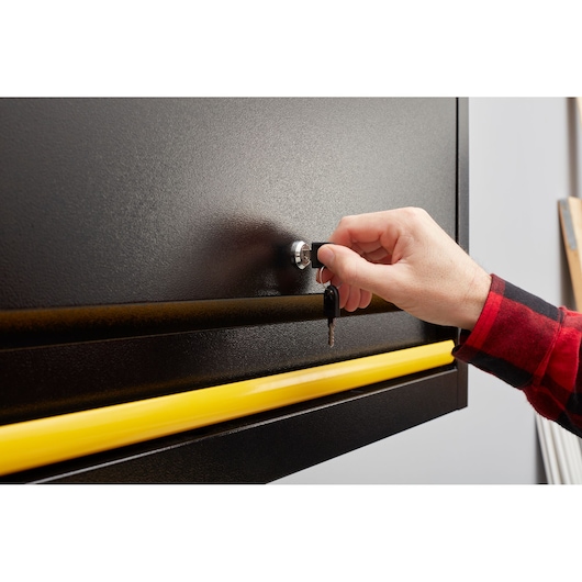 STANLEY STST97599-1 black toolbox front angle, hand turning key in lock, yellow handle visible.