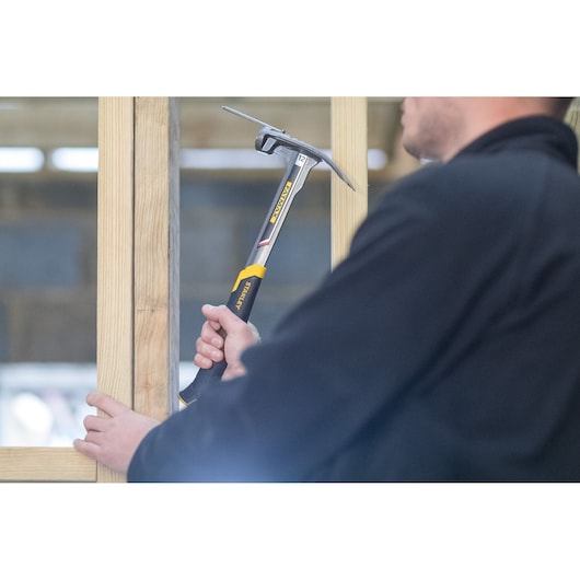 STANLEY XTHT0-51123 framing hammer in use, yellow and black handle, held against wooden beams.